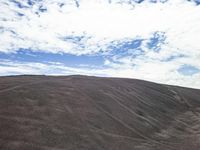 a hill is covered in lots of sand on an overcast day with clouds in the background