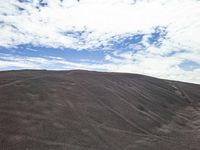 a hill is covered in lots of sand on an overcast day with clouds in the background