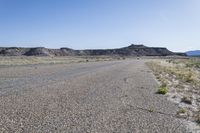 a gravel road running between some hills with a blue sky in the background behind it