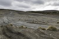 a gravel road surrounded by dry grass and shrubs in the desert under a cloudy sky