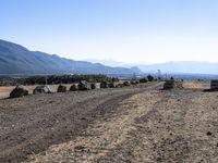 a long gravel road with rocks along side it and mountains beyond it, in the distance are hills