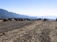 a long gravel road with rocks along side it and mountains beyond it, in the distance are hills