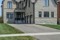 a gray and brick house on the corner of a sidewalk with grass in front of it