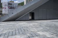 an image of a gray building in the city with a stairs outside the door and on a brick area with the buildings behind it