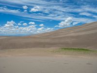 a person is standing outside in the desert with some grass in the desert and some clouds in the sky