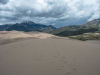 the sand dune is covered by a huge cloud cover and has tracks on the sand