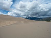 a desert landscape that looks like a giant sand dune in the background is large mountains