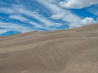 two people walking through an arid area of sand dunes with a sky background and sparse, cloud covered hills