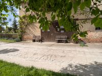 some benches near an old building with a brick wall and two doors behind it and a tree