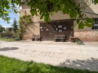 some benches near an old building with a brick wall and two doors behind it and a tree