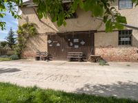 some benches near an old building with a brick wall and two doors behind it and a tree