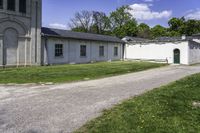 a paved path winds through a grassy area next to an old building with two green doors