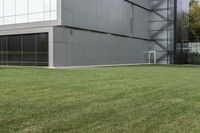 a man sitting on top of a green field next to an apartment building with glass walls