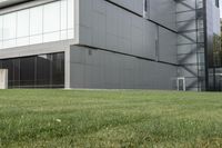 a man sitting on top of a green field next to an apartment building with glass walls