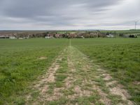 green field with an unpaved path leading to the small town below the horizon