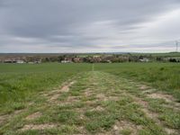 green field with an unpaved path leading to the small town below the horizon