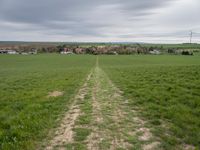 green field with an unpaved path leading to the small town below the horizon