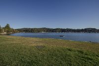 the sun shines brightly on a green field by a river surrounded by trees with several boats in the water and a blue sky above