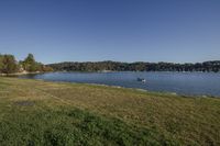 the sun shines brightly on a green field by a river surrounded by trees with several boats in the water and a blue sky above