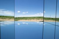 there is a mirror view of a blue sky with clouds and a field behind it