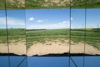 there is a mirror view of a blue sky with clouds and a field behind it