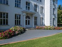 a garden is in the foreground with flowers around it and walkway leading up to the front of a white house