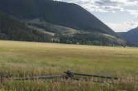 the grassy field has a fence that is next to a mountain range, with mountains in the distance