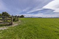 grass and fenced in area of grassy field under blue sky with clouds above it