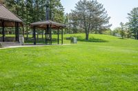 gazebo and benches in open park with grass, trees, and woods behind it