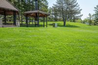 gazebo and benches in open park with grass, trees, and woods behind it