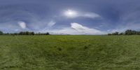 a green grassy field with mountains in the background and clouds over the grass is in a circular panorama format