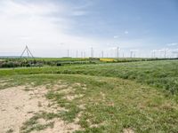 windmills in a grassy field under blue sky with some clouds and water in the distance