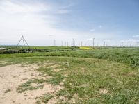 windmills in a grassy field under blue sky with some clouds and water in the distance