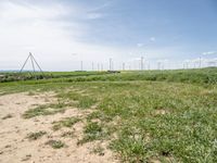 windmills in a grassy field under blue sky with some clouds and water in the distance