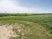 windmills in a grassy field under blue sky with some clouds and water in the distance