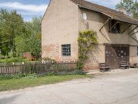 an old brick building with a few bushes and other decorations on it next to a small road