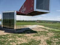 a couple of big shipping containers sitting in a field of grass near a road and a body of water