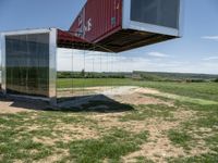 a couple of big shipping containers sitting in a field of grass near a road and a body of water