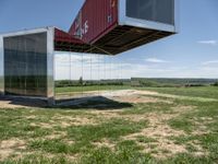 a couple of big shipping containers sitting in a field of grass near a road and a body of water