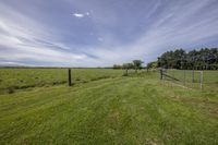 a grassy pasture with an open fenced in field next to it and clouds overhead