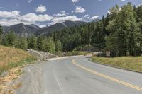 a scenic road is lined by lush green trees and mountains in the distance, on a sunny day