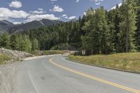 a scenic road is lined by lush green trees and mountains in the distance, on a sunny day