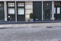 an empty street with an outside bench and green doors on it with windows and planters