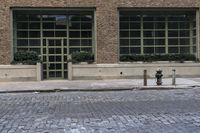 two fire hydrants on the sidewalk in front of a large brick building with many windows