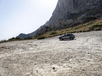 a grey car is parked by the side of a mountain in front of some rocks