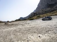 a grey car is parked by the side of a mountain in front of some rocks