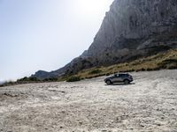 a grey car is parked by the side of a mountain in front of some rocks