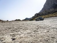 a grey car is parked by the side of a mountain in front of some rocks