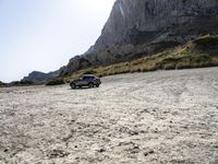 a grey car is parked by the side of a mountain in front of some rocks