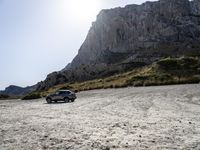 a grey car is parked by the side of a mountain in front of some rocks